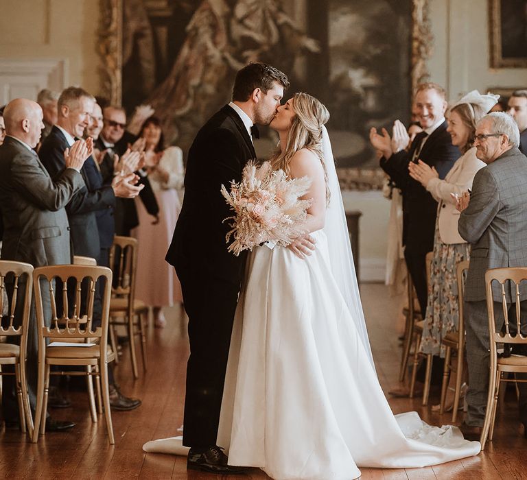 Doddington Hall and Gardens country house wedding venue with the bride and groom sharing their first kiss as a married couple underneath a crystal chandelier 