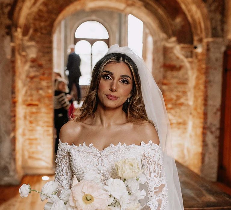 Bride in delicate lace long sleeve off the shoulder Eva Lendel wedding dress holding pastel yellow and white bouquet with giant poppies 