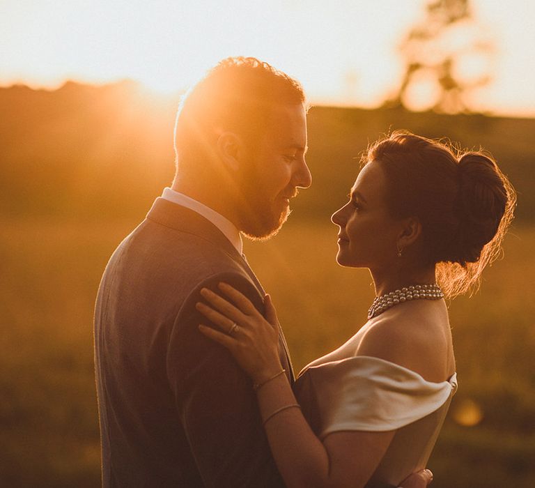 Bride in elegant pearl choker necklace in off the shoulder wedding dress with groom during the sunset 