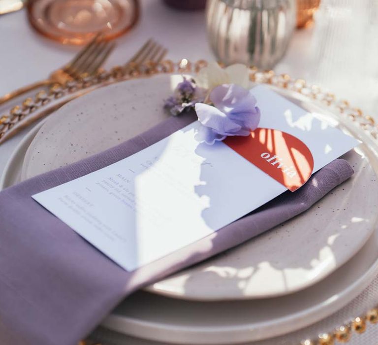 Lilac wedding napkin on gold rimmed plate with minimalist wedding menu and deep orange name place card