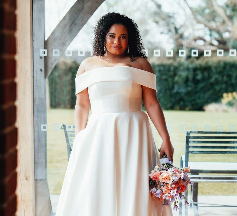 Bride in off the shoulder wedding dress with puddle train holding orange, lilac and peach mixed flower bridal bouquet 