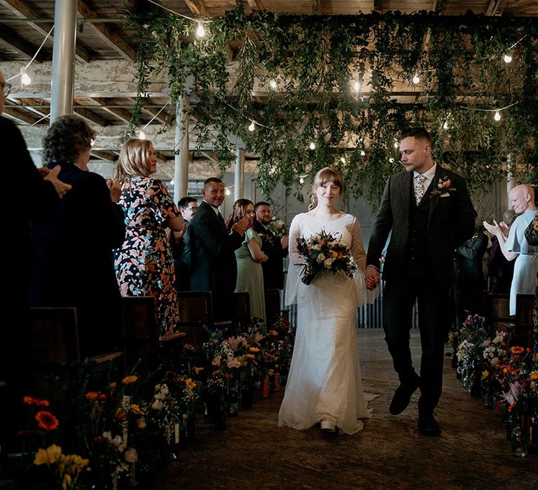 Bride in dotted wedding dress with platform shoes walking hand in hand with the groom in a grey suit at industrial wedding 