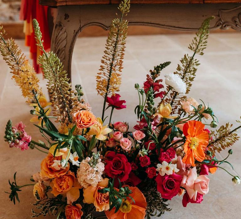 Seasonal wedding flower arrangement with pink and orange garden roses, orange floribunda, yellow ranunculus flowers, foliage and Iceland poppies 