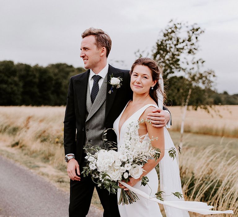 Bride in plunging Made With Love wedding dress holding white wedding bouquet with groom in three piece suit 