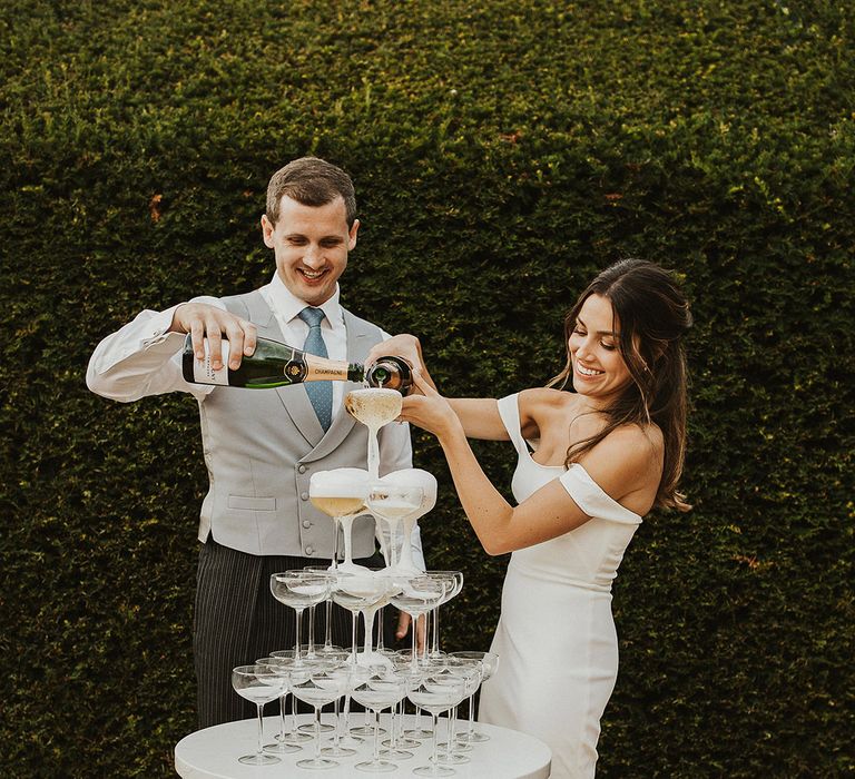 The bride and groom with their classic champagne tower decoration with bride in off the shoulder Halfpenny London wedding dress 