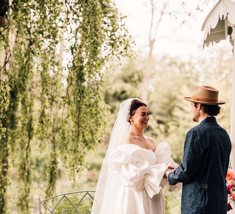 An outdoor wedding at Preston Court in Kent with the bride and groom holding hands at the altar 