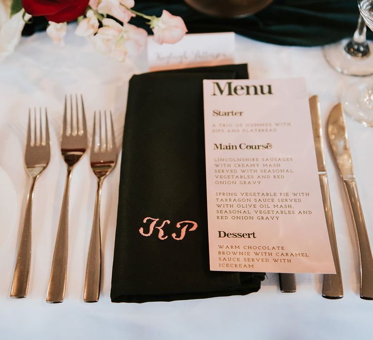 Wedding menu on black napkin surrounded by gold wedding cutlery 