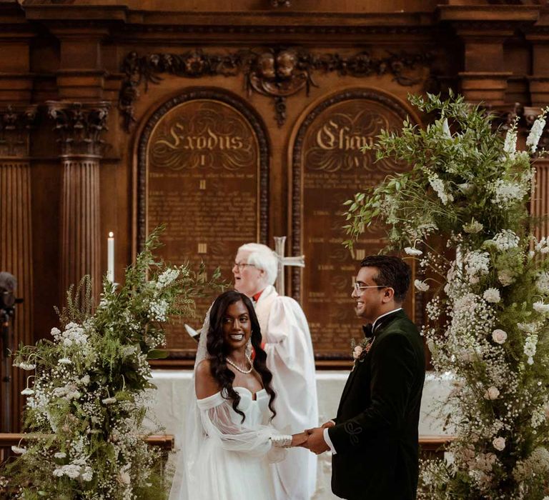 Bride in off the shoulder layered tulle wedding dress and groom in bottle green velvet grooms suit, black bowtie and chic boutonniere at the alter of Inner Temple Hall vow renewal 