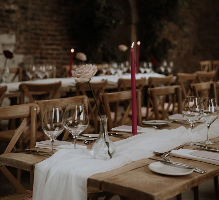 Romantic red and pink wedding table decorations with white table runner, bud vases, and dark pink candles 