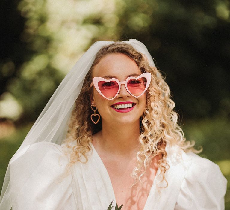 Bride in puff sleeve wedding dress by Watters with pale pink retro sunglasses and veil accessories 