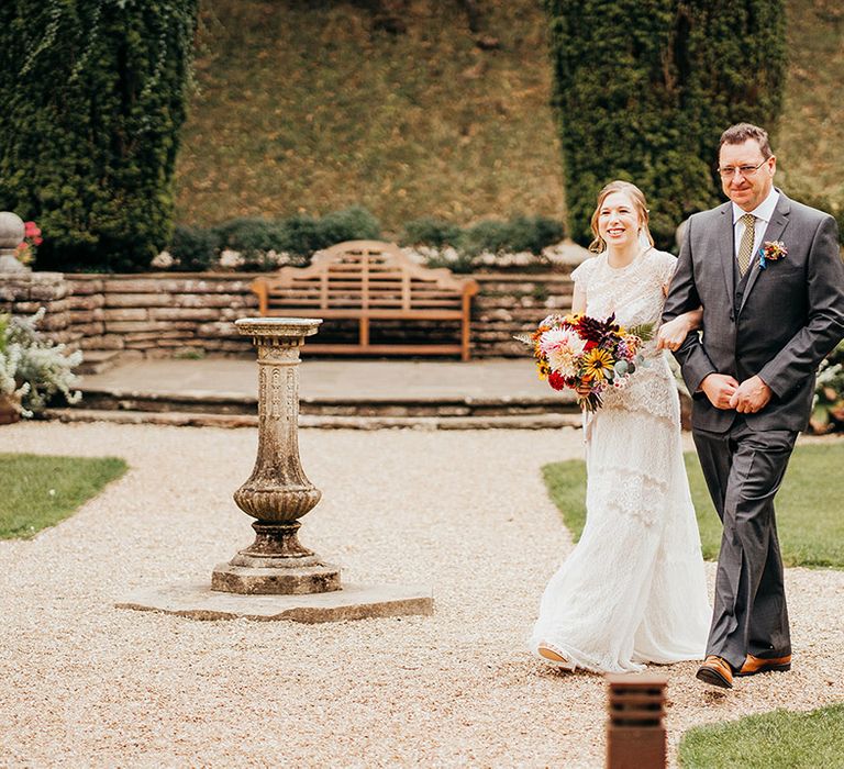 Father of the bride walks down the aisle with the bride at outdoor wedding 