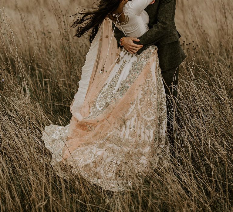 Bride in white and gold sparkly lehenga kissing groom in fields of Yorkshire countryside 