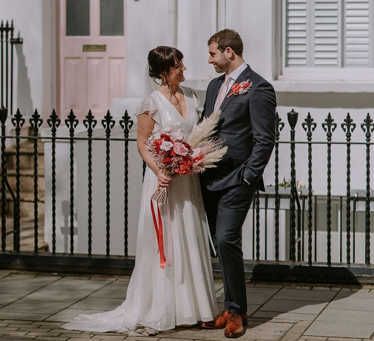 Bride and groom stand in front of building with a pastel pink front door that matched the red and pink wedding theme 