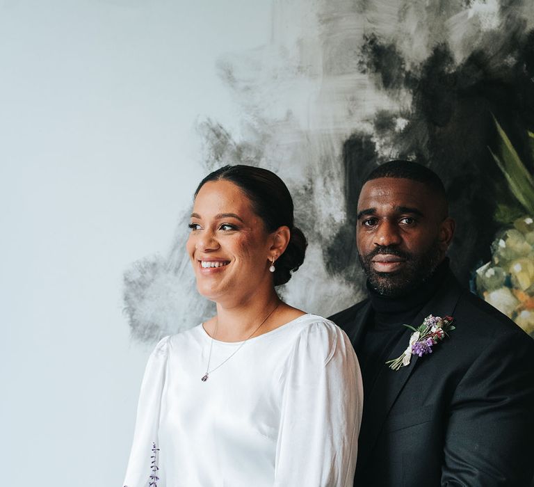 Groom in black suit embracing the bride in a long sleeve satin wedding dress 