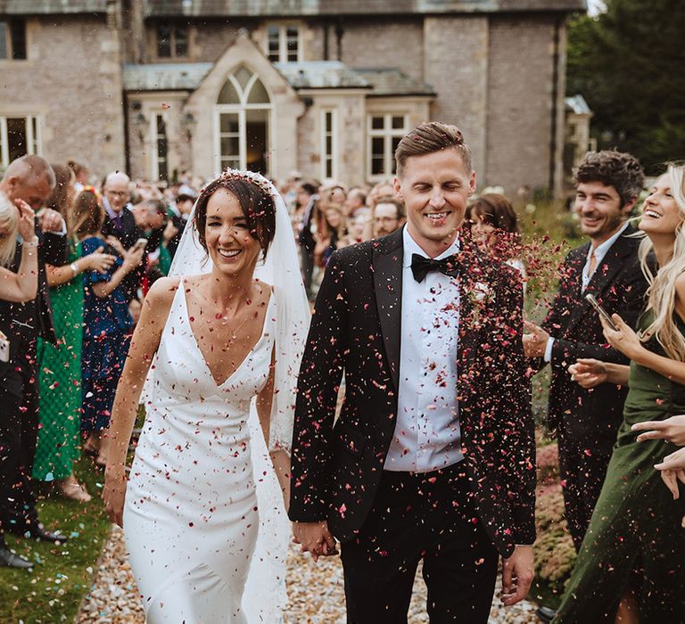 Bride in slip gown walking hand in hand with the groom in black tie 