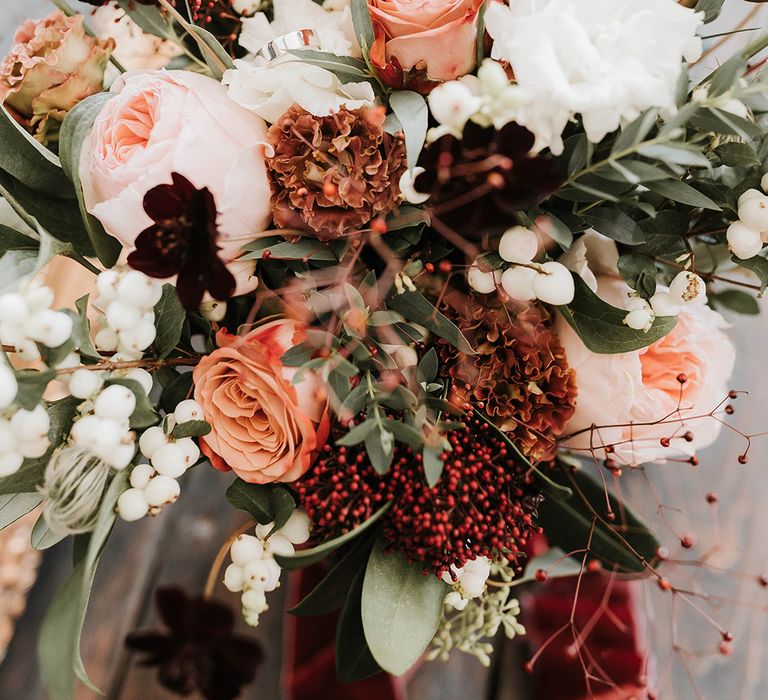 Peach, red and white winter wedding bouquet with a thick diamond wedding band 