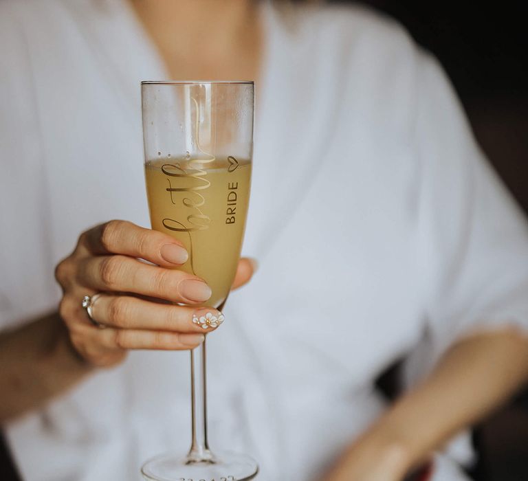 Bride with floral nail art drinking mimosa showing off engagement ring on wedding day 