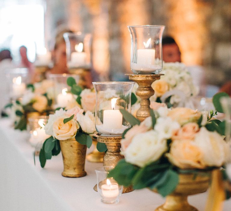 Gold vases and candleholders with pillar candles and peach flowers decorating the top table 