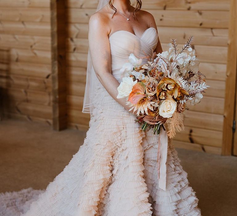 Bride wears a strapless ruffle wedding dress with sweetheart neckline carrying boho autumn wedding bouquet 