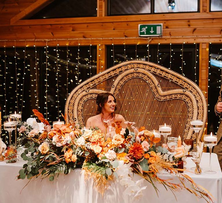 Groom reads out his wedding speech standing next to the sweetheart table with double peacock chair for boho wedding 