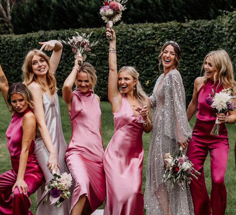 Bride wearing a silver sequin gown posing for a picture with her bridesmaids with mismatched pink dresses