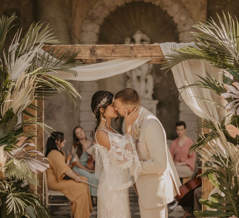 Groom in beige Suit kissing his bride in a lace wedding dress