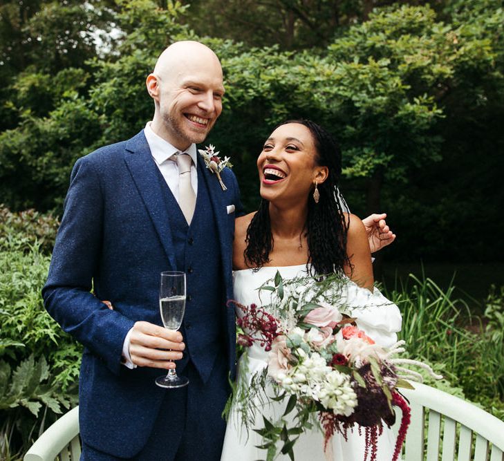 Groom in blue wool suit and bride in off the shoulder dress smiling 