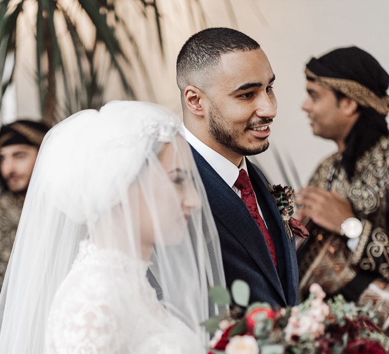 Bride in navy suit and maroon tie smiling at intimate wedding ceremony 