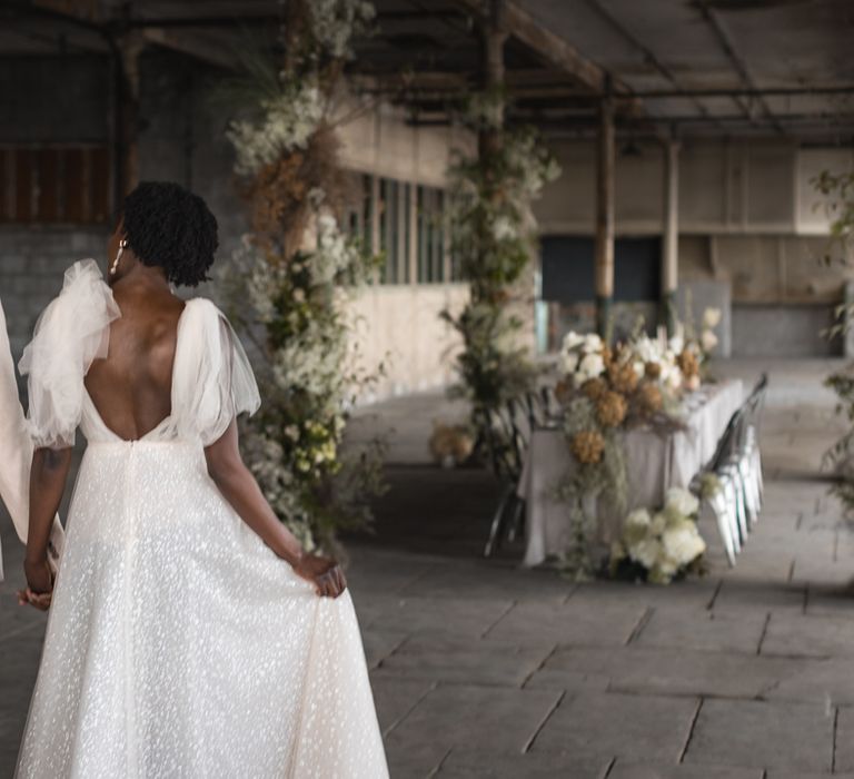 Bride in sparkly wedding dress and groom in beige suit entering their industrial wedding venue 