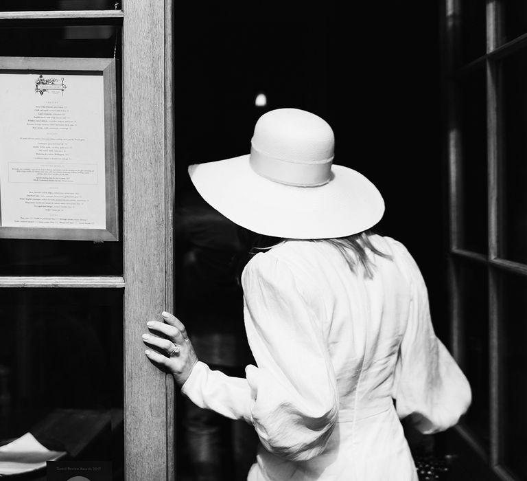 Bride wearing puff sleeve wedding dress and white wedding hat walking into wedding venue - black and white photography 