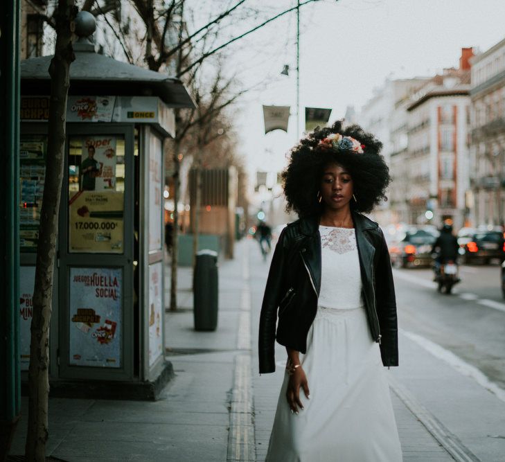 A bride with alarge afro walks down the street in a leather jacket and wedding dress.