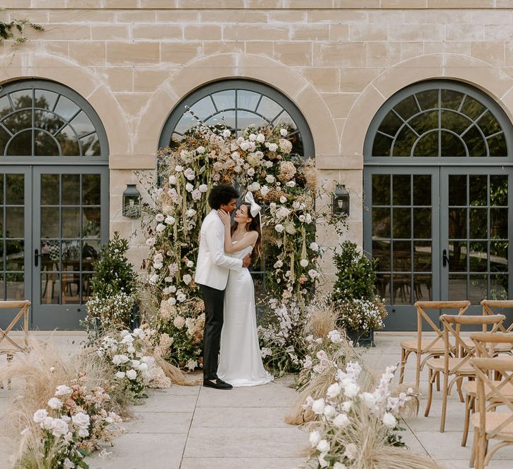 Bride and groom standing at the altar with a floral arch and flower lined aisle 