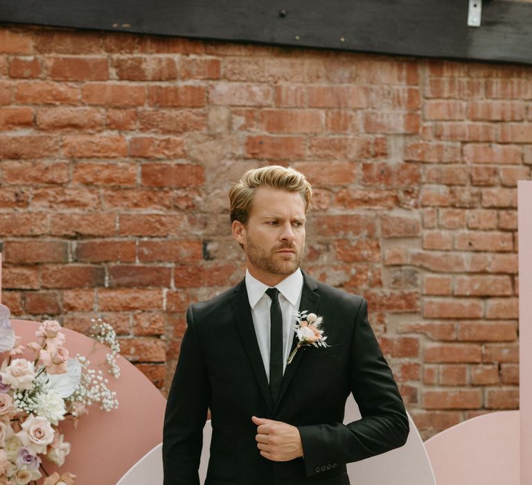 Groom in a black suit with pastel buttonhole standing at the altar of The Shack Revolution