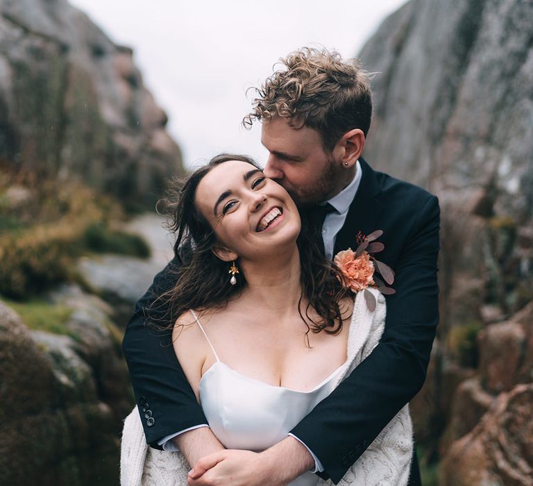 The bride and groom hug among the rocky coastal landscape