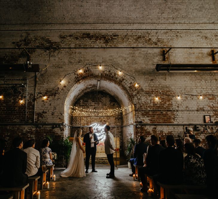 Industrial venue shot of couple's wedding ceremony with lights as backdrop