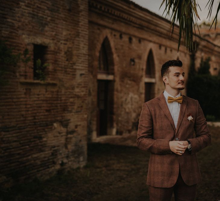 Stylish groom in a brown wedding suit with check pattern and ochre bow tie for autumn wedding 