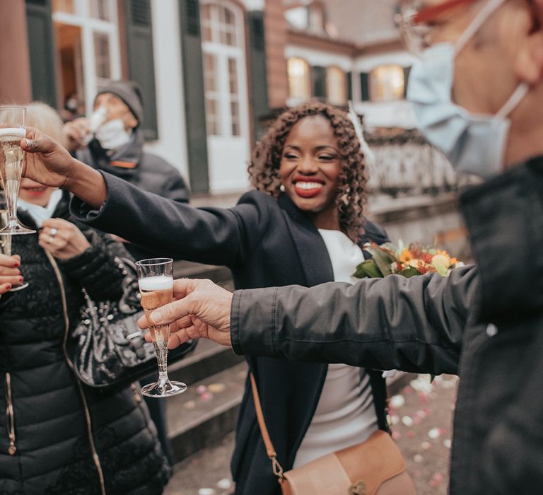 Bride holds out glass of champagne outside after marrying