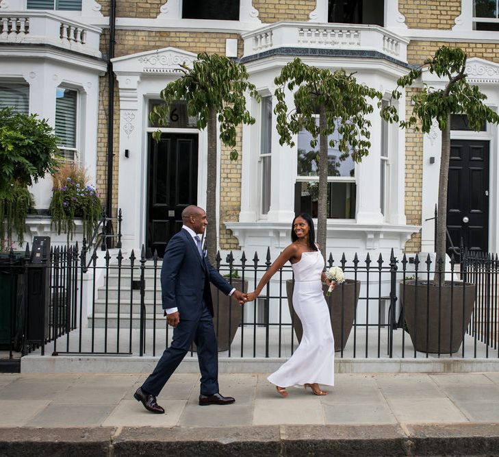 Bride and groom holding hands in a navy suit and one shoulder Roland Mouret dress walking the streets of Chelsea