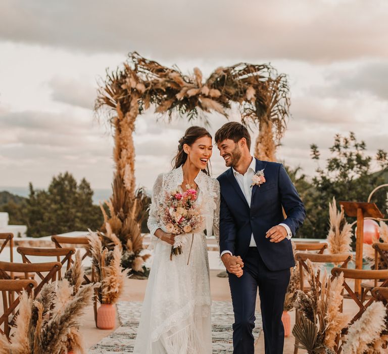 Boho bride and groom descending up the aisle in a lace Marylise Bridal gown and navy suit 