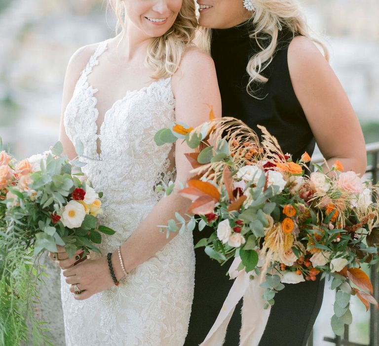 The brides holding their orange bouquets, wearing a white wedding dress and black jumpsuit