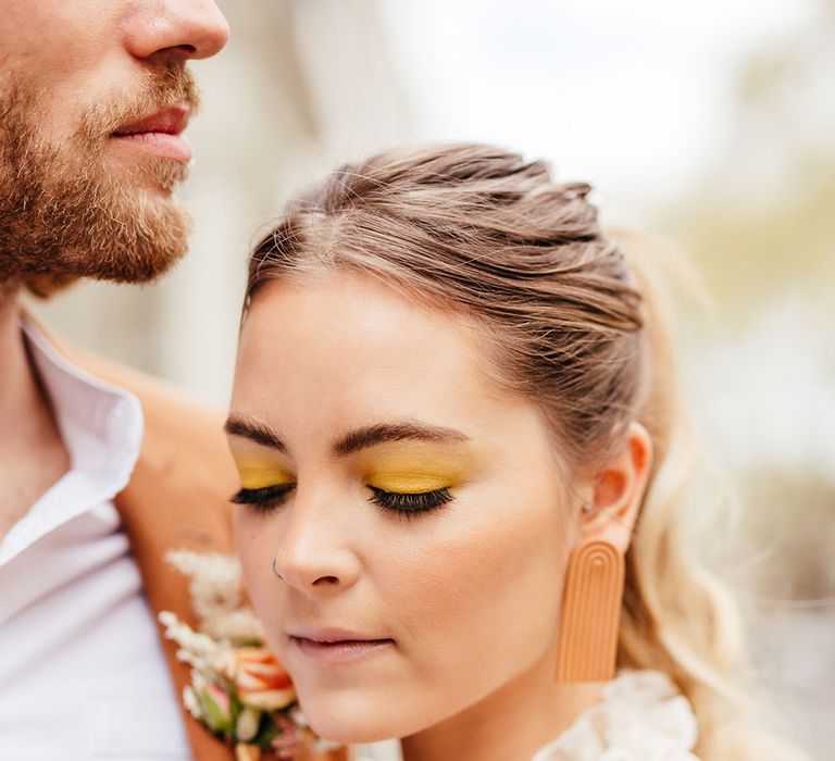 Bride with yellow wedding eyeshadow, sleek back ponytail and retro earrings 