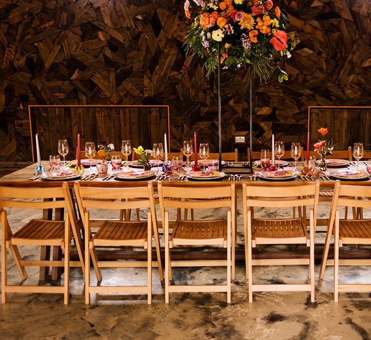 Wooden table at rustic barn reception with colourful flowers and tableware decor 