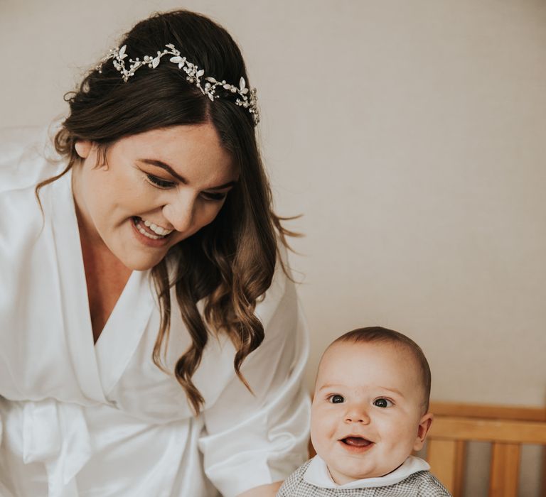 Bride sits with her baby on the morning of her wedding as she wears white silk robe