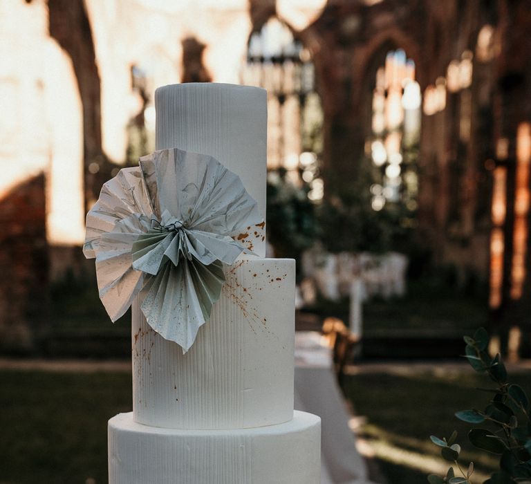 Tall three-tier wedding cake on a white cake stand with fan design 