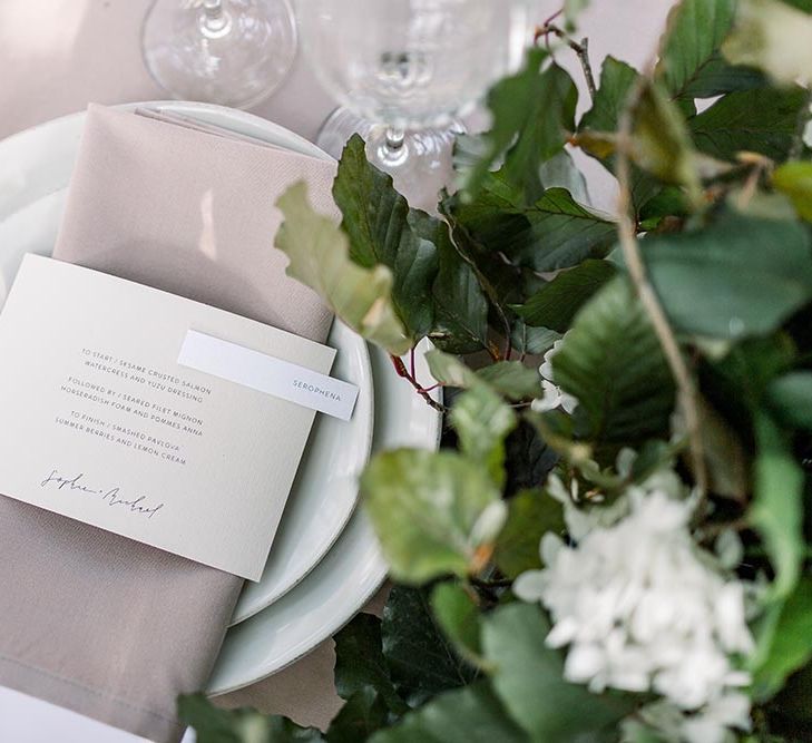 Place setting with white tableware, beige napkin and contemporary menu card