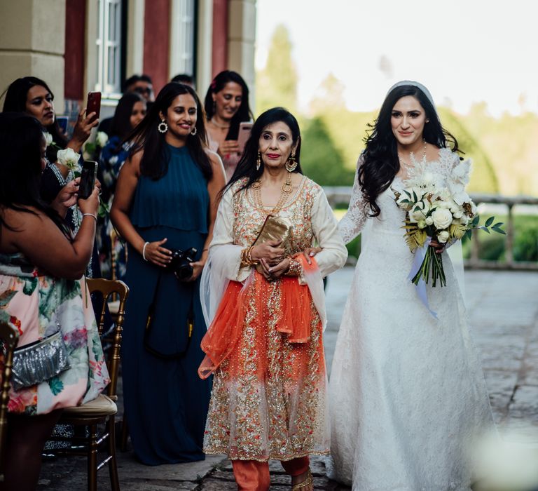 Bride walks down the aisle with her mother who wears a bright and colourful saree