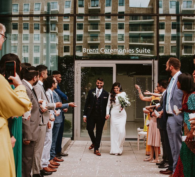 Confetti moment at Brent Civic Centre wedding venue with bride in a long sleeve fitted wedding dress and groom in a floral tie 