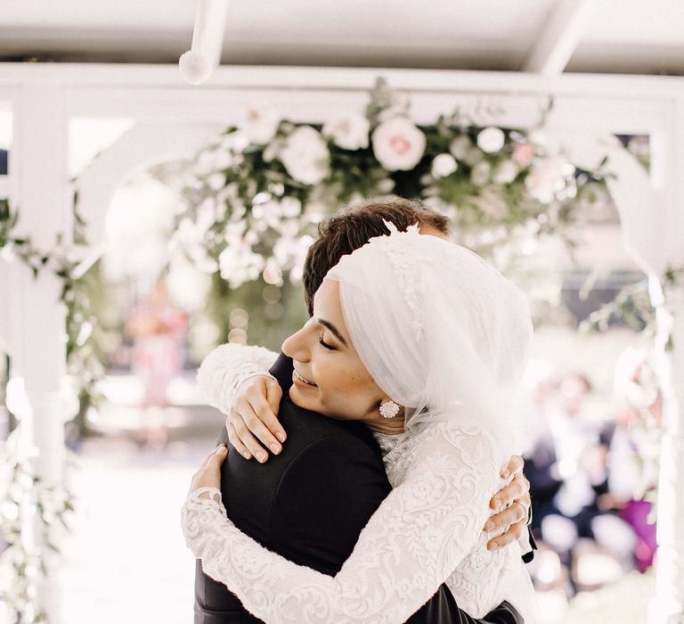 Bride and groom embrace with bride wearing beaded flower earrings and bridal hijab