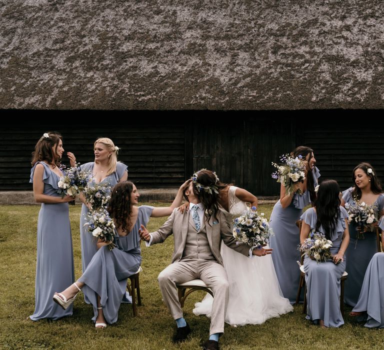 Bride & groom sit with bridesmaids and have funny photo for their post-wedding pictures in field