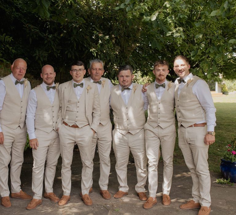 Groom and groomsmen in beige suits, waistcoats and sage green bow ties 